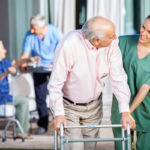 Happy Caretaker Assisting Senior Man In Using Zimmer Frame