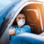 Young woman driving car with protective mask on her face.  Healthcare, virus protection, allergy protection concept.