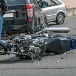 broken motorcycle closeup beside the car. an accident on the road in the city on a sunny day involving a motorcycle and a car.